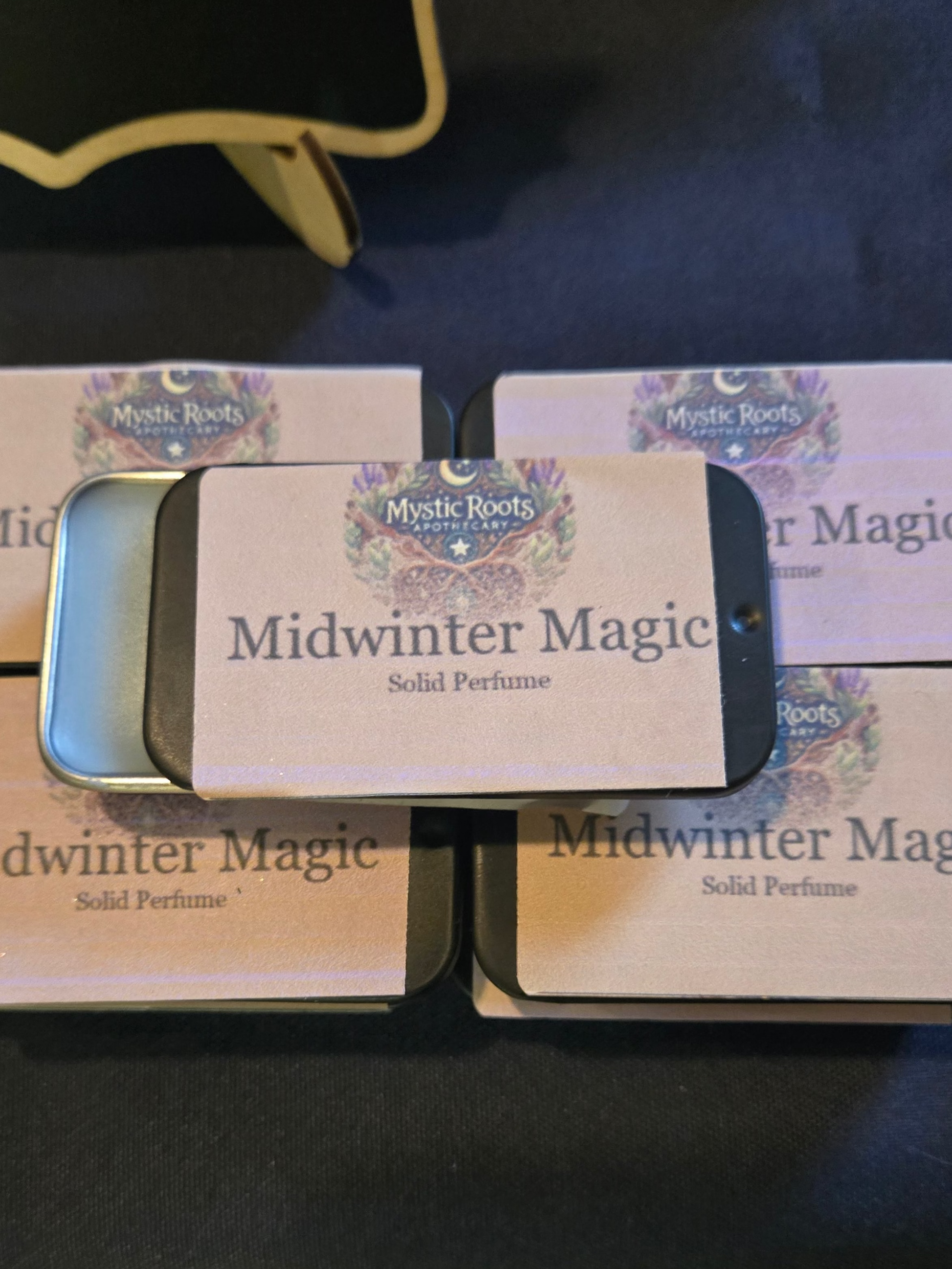 Four boxes of 'Midwinter Magic' solid perfume on a dark surface.